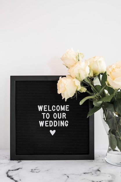 Foto gratuita lavagna nera con benvenuto al nostro messaggio di matrimonio e vaso rosa sul piano del tavolo in marmo