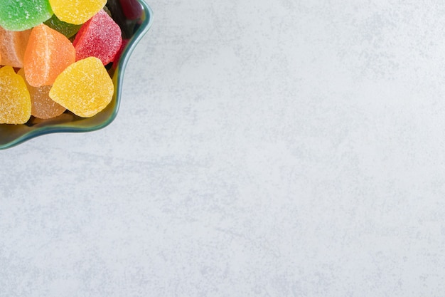 Black bowl of colorful jelly marmalades on marble background.