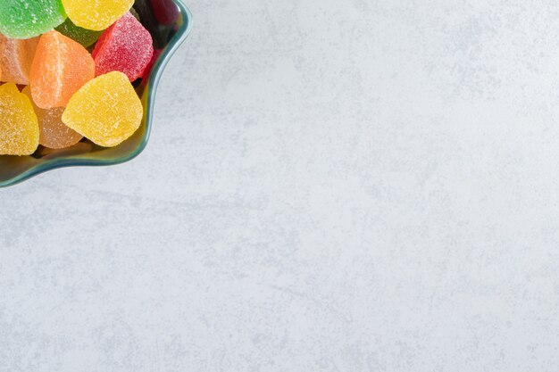 Black bowl of colorful jelly marmalades on marble background.