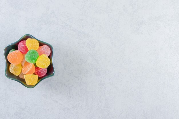 Black bowl of colorful jelly marmalades on marble.