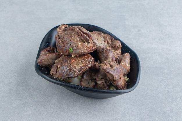 Free photo a black bowl of delicious meat on marble background.