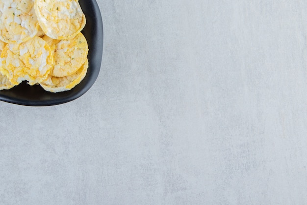 Free photo black bowl of delicious rice chips on stone.