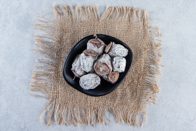 Black bowl of dried persimmon fruits on marble background