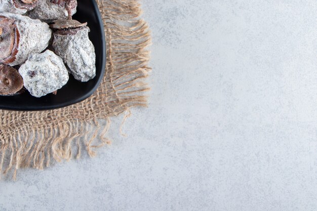 Black bowl of dried persimmon fruits on marble background.