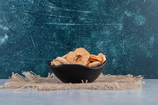 Black bowl of healthy dried apple rings on stone background.