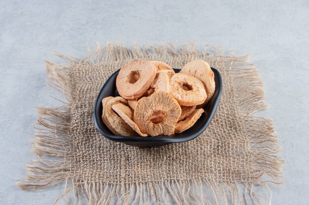 Black bowl of healthy dried apple rings on stone background.