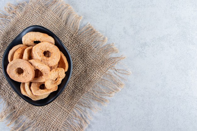 Black bowl of healthy dried apple rings on stone.