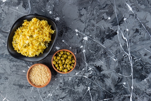 Free photo black bowl of saffron rice and green peas on marble background.