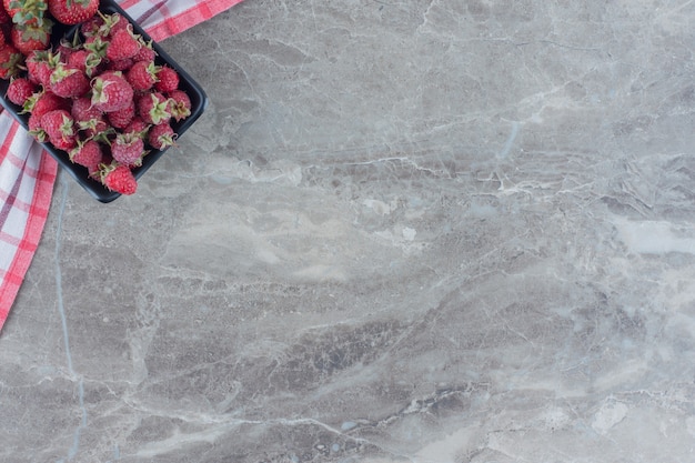 Black bowl of strawberries and raspberries on a tablecloth on marble.