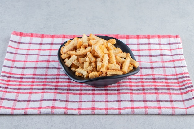 Black bowl of tasty crunchy crackers on stone background.