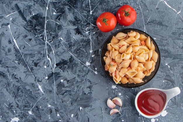 Black bowl of tasty seashell pasta with ketchup on marble surface. 