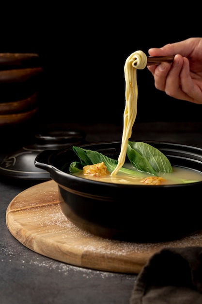 Бесплатное фото Черная миска с супом с лапшой на деревянной тарелке