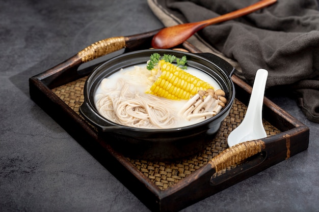 Black bowl with noodles and mushrooms with corn on a wooden table