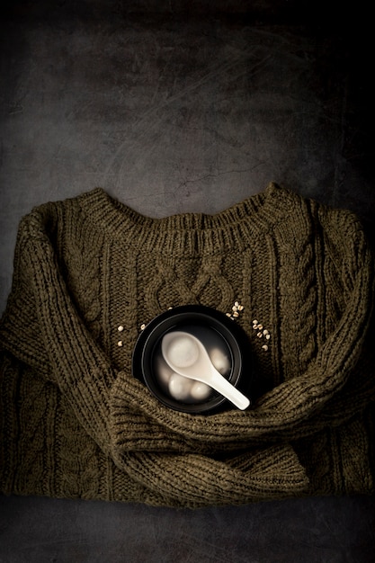 Free photo black bowl with soup on a green sweater on a grey background