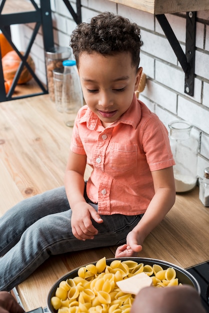 Free photo black boy near pan with pasta showing thumb up