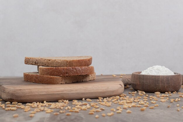 Black bread slices and bowl of flour on marble surface. High quality photo