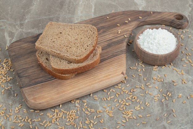 Black bread slices and bowl of flour on marble surface. High quality photo