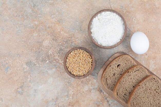 Black bread slices, flour, barley and eggs on marble surface