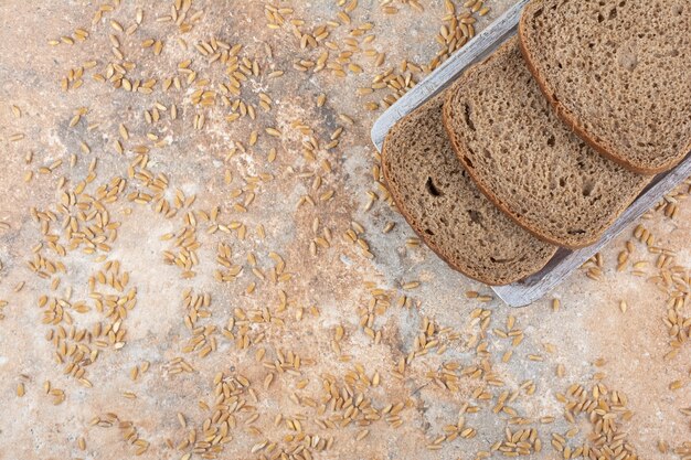 Black bread slices with barley grains on marble surface