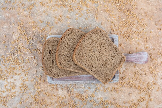 Black bread slices with barley grains on marble surface