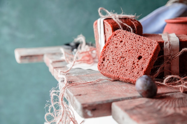 Black bread slices wrapped with white paper and plums on a wooden table.