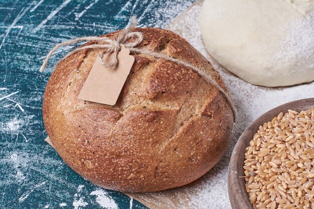 Black bread on wheat grains on blue table.