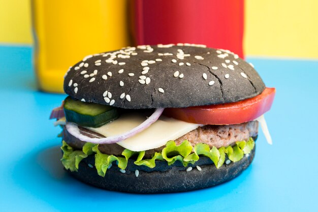 Black burger on blue table with bottles behind