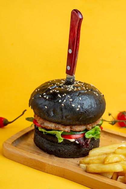 Free photo black burger with knife inside and fries