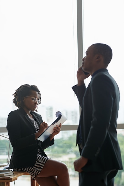 Free photo black businessman talking on phone and female colleague writing on notepad