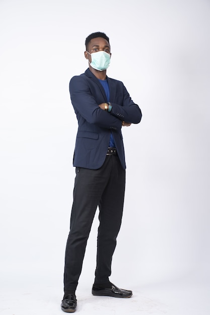 Black businessman wearing a suit and face mask standing with arms crossed - the new normal concept