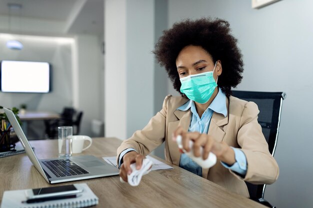 Черная деловая женщина дезинфицирует офисный стол во время пандемии коронавируса
