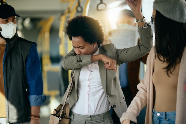 Free photo black businesswoman sneezing into elbow while commuting to work by bus