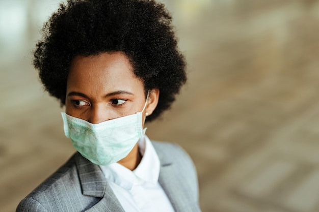 Foto gratuita donna d'affari nera che indossa una maschera protettiva sul viso mentre si trova nel corridoio pubblico