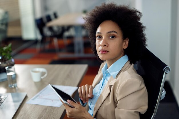 Black businesswoman working on digital tablet in the office and looking at camera