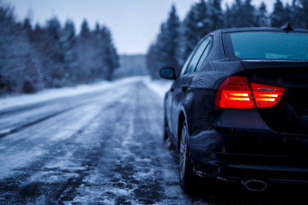 Black car on an iced road surrounded by trees covered with snow