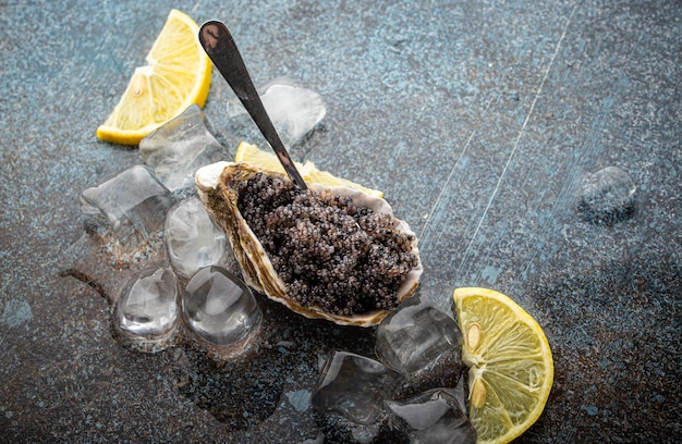 레몬 웨지와 얼음 조각이 든 숟가락으로 굴 껍질에 담긴 블랙 캐비어