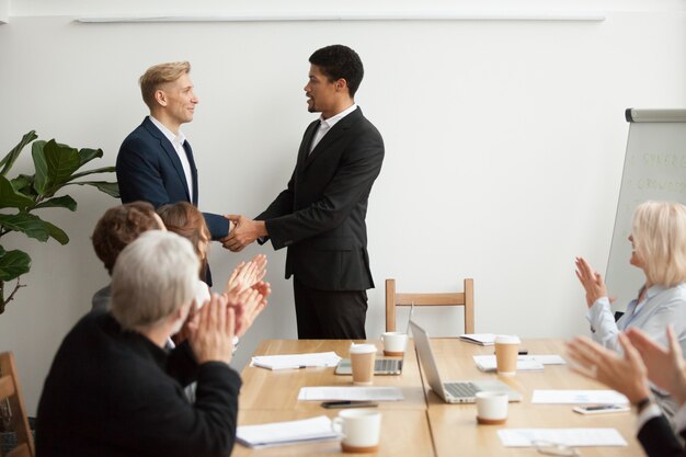 Black ceo and white businessman shaking hands at group meeting