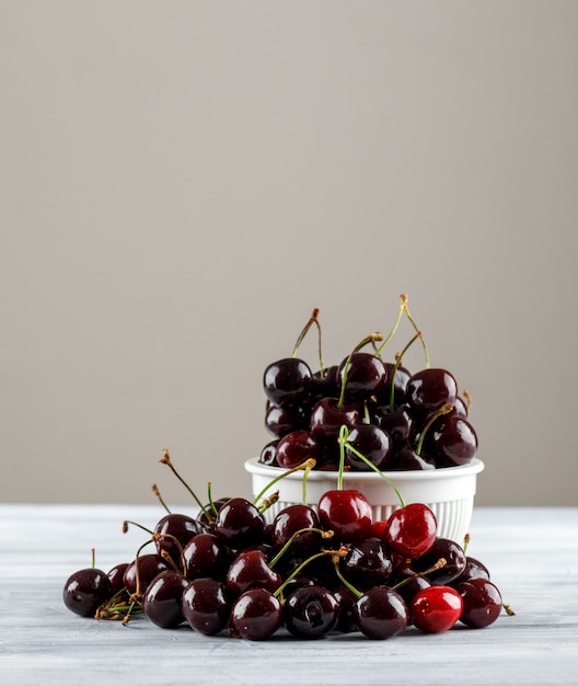 Black cherries in a bowl on grungy and grey gradient surface. side view.