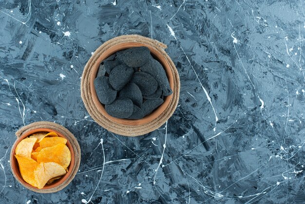 Black chips and potato chips in bowl on trivets , on the marble table. 