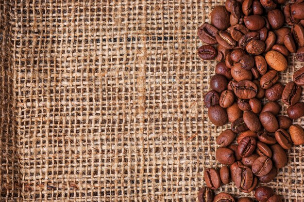 Black coffee beans in burlap sack on wooden table,