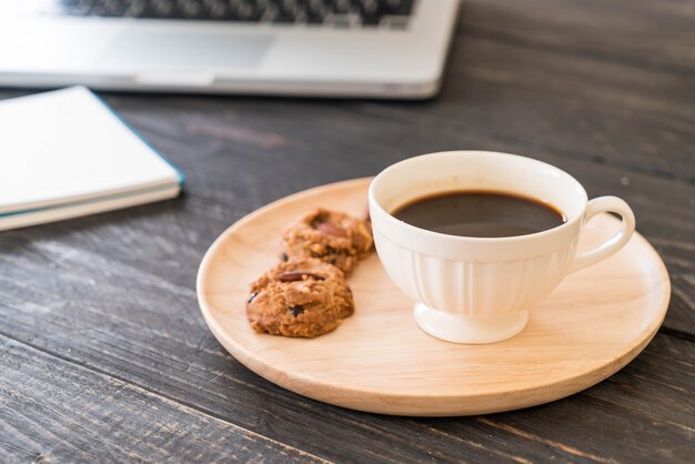 ラップトップとノートブックを備えたブラックコーヒーとクッキー