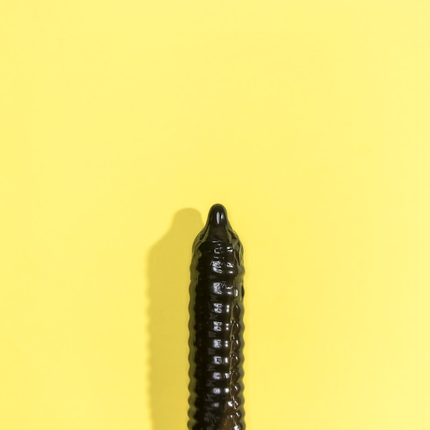 Black condom on yellow background with copy-space