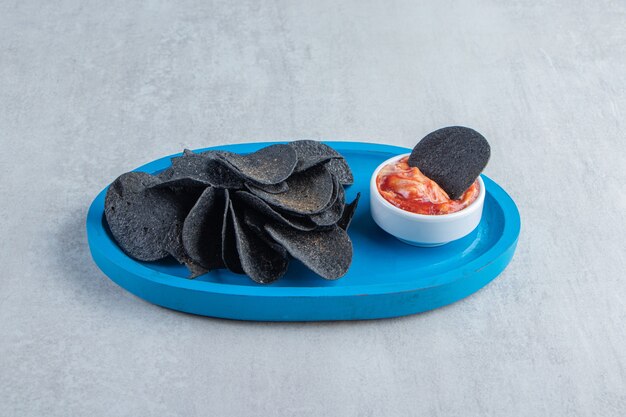파란색 접시에 검은색 바삭한 칩과 특별 소스.