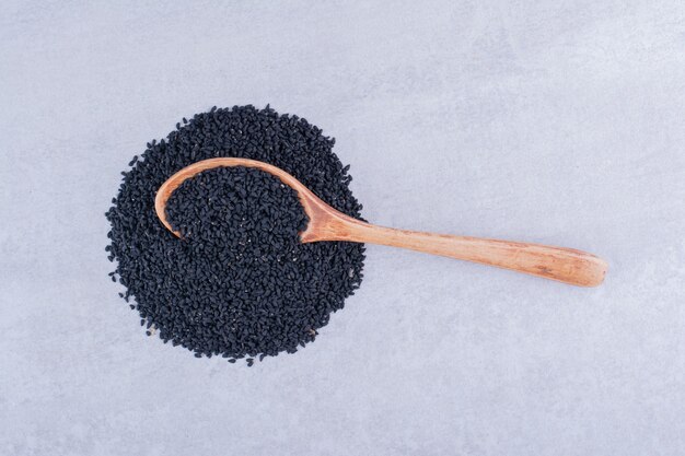 Black cumin seeds in a wooden spoon on concrete surface