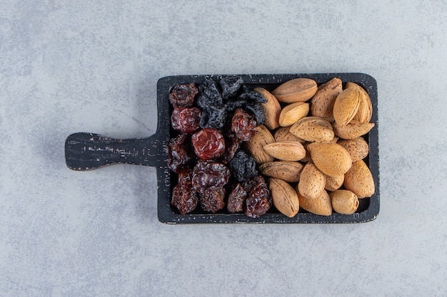 Black cutting board full of dry dates and nuts on stone background.