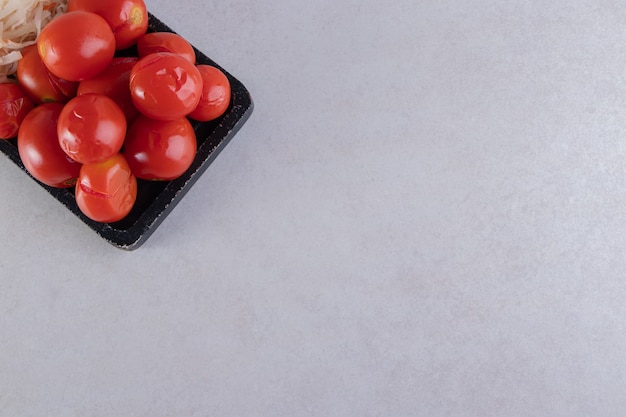 Free photo black cutting board of pickled tomatoes and cabbage on stone.