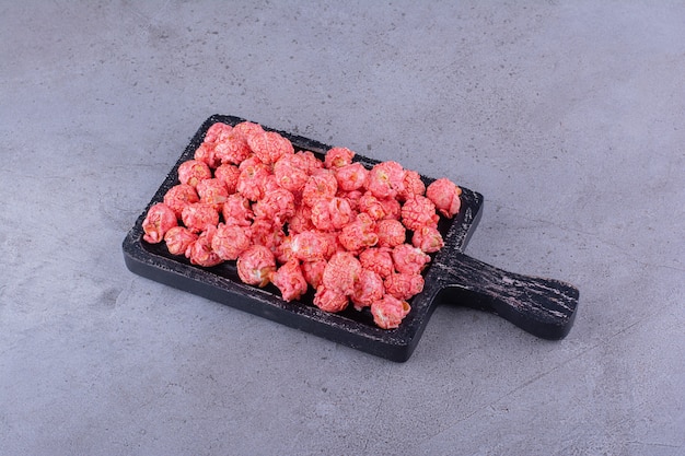 Foto gratuita tagliere nero di palline di popcorn rosa su superficie in pietra