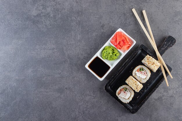 Black cutting board of sushi rolls with sesame seeds on stone background. 