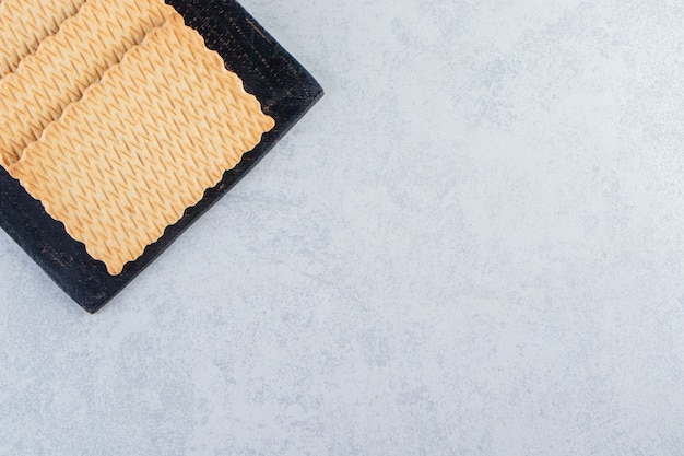 Black cutting board of tasty biscuits placed on stone background.