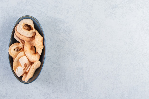 A black deep plate with healthy dried apples on stone background.